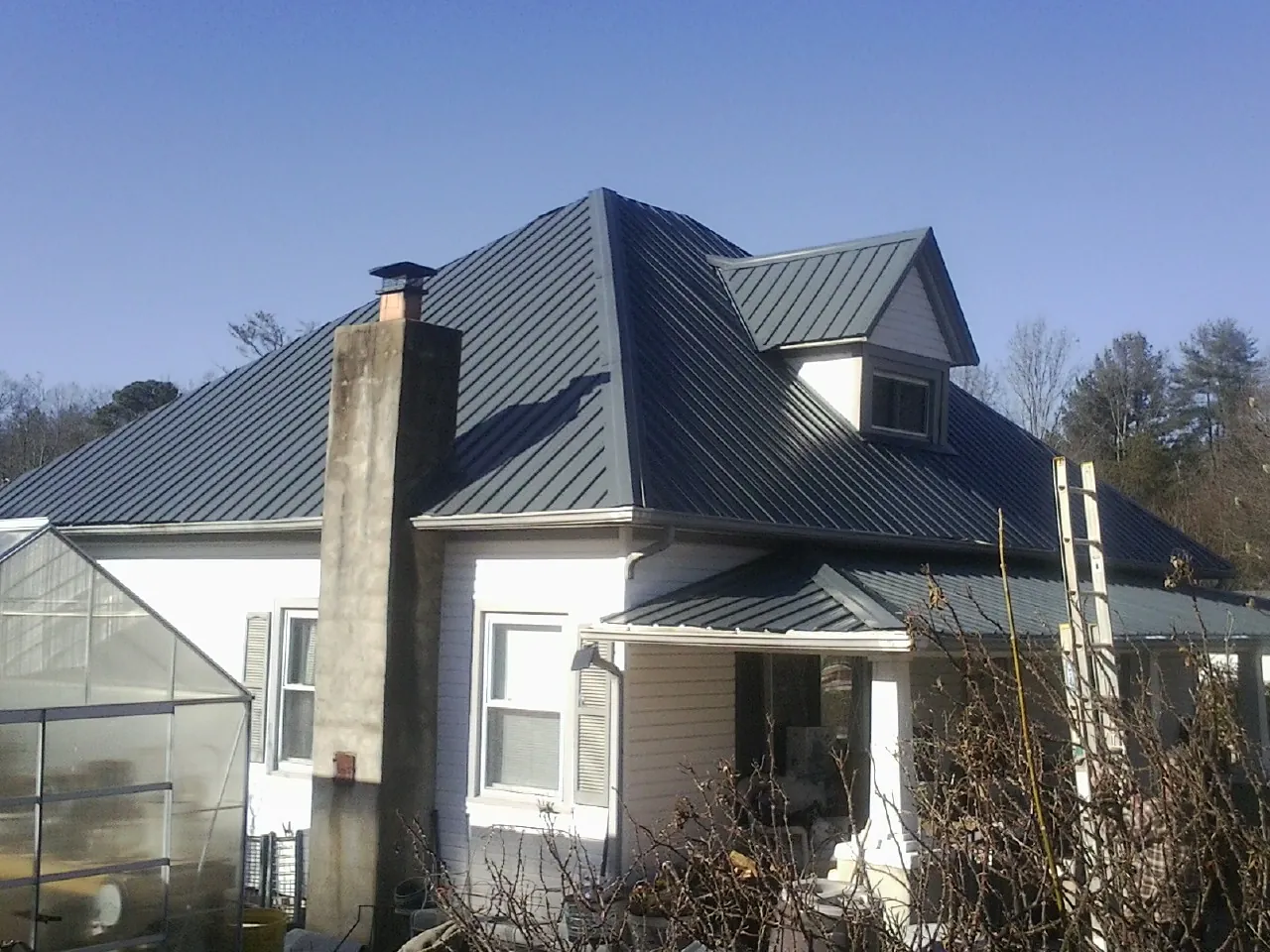 Dark blue standing seam metal roof on a white farmhouse with dormer — Slate & Tile Roof Repair by Roofing Brothers in Richburg
