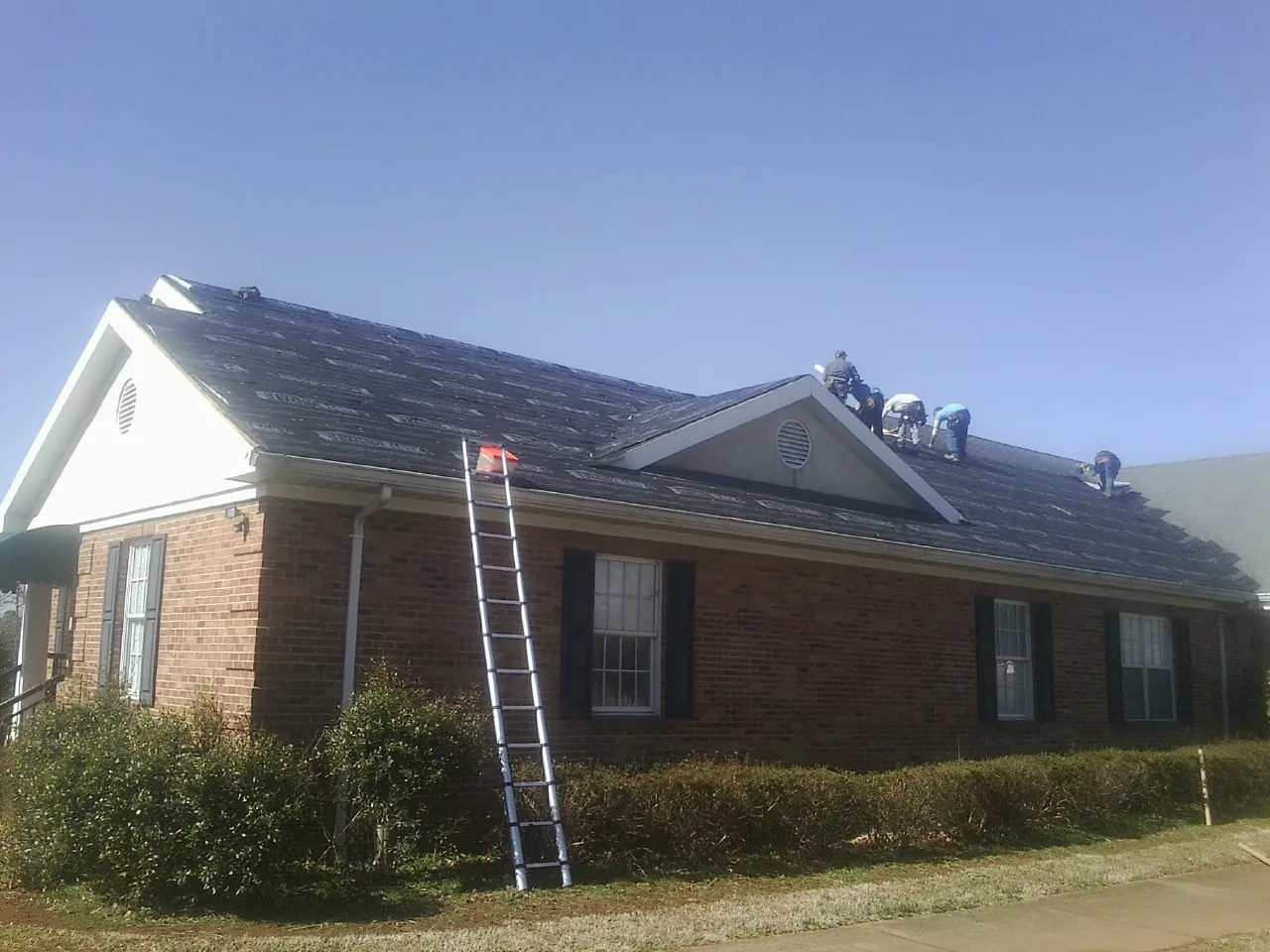 Crew tearing shingles off a brick ranch roof with a ladder set — Emergency Roof Repair work by our crew in Richburg