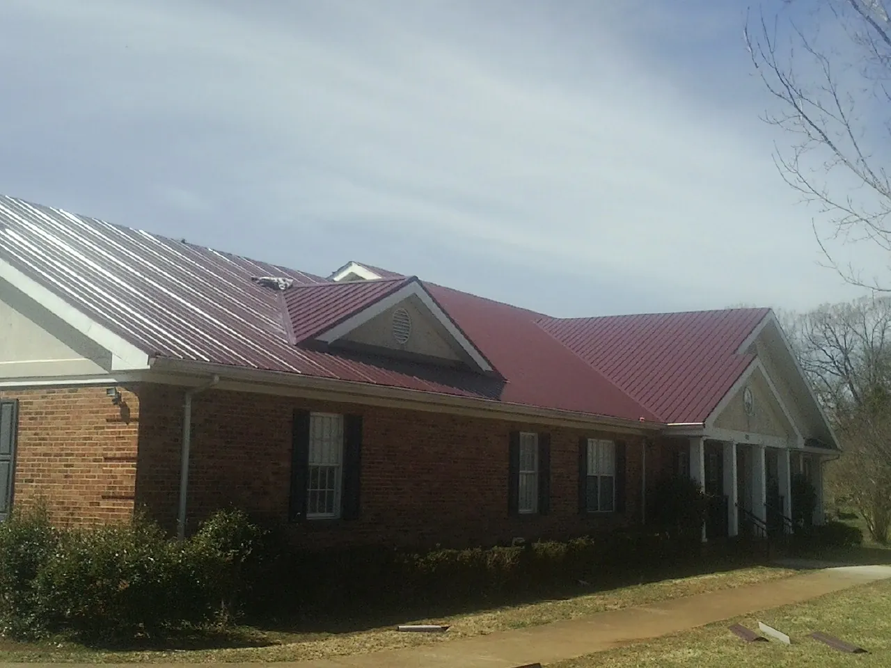 Red metal roof with gabled entries on a long brick building, from a Hail Damage Roof Repair job in Richburg