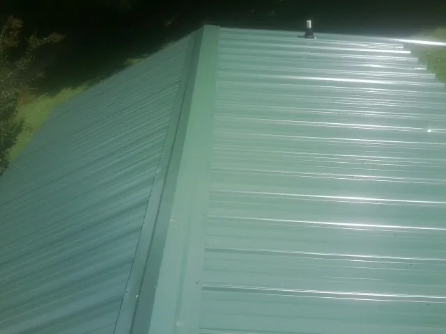 New green metal panels meeting at the ridge of a roof — Flat Roof Repair work by our crew in Richburg