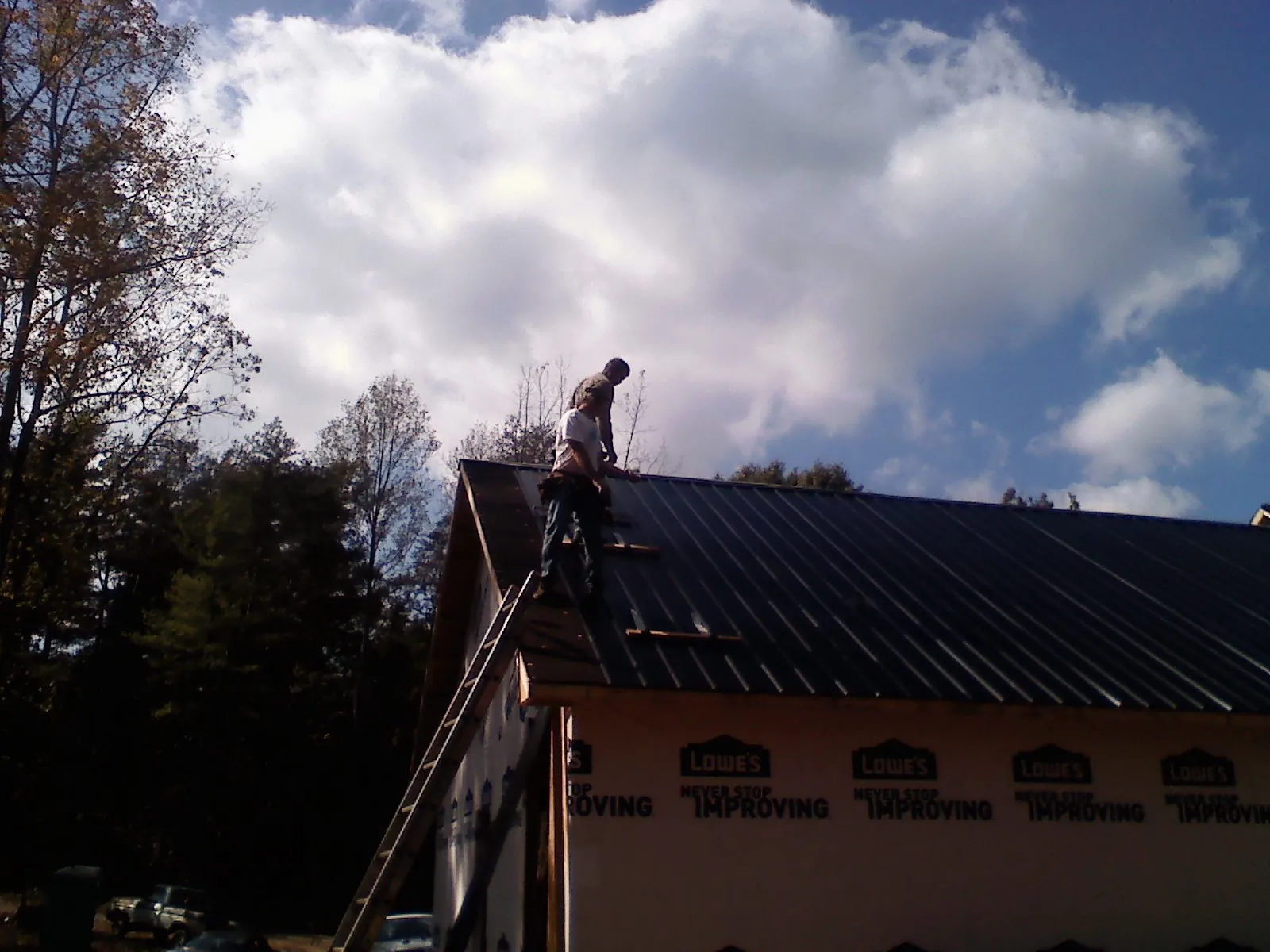 Roofer fastening dark metal panels high against a cloudy sky, from a Roof Inspection job in Richburg