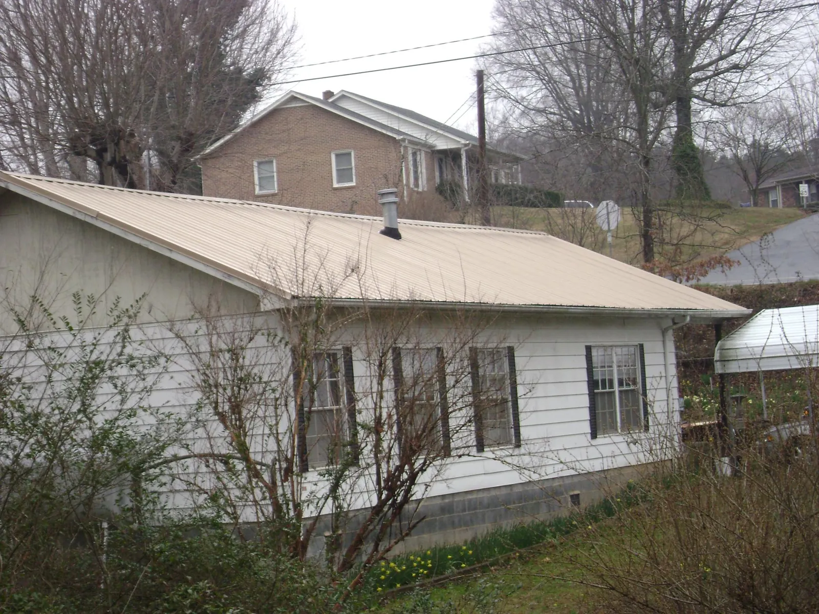 Tan metal roof on a white sided house set into a hillside — Commercial Roofing by Roofing Brothers in Richburg