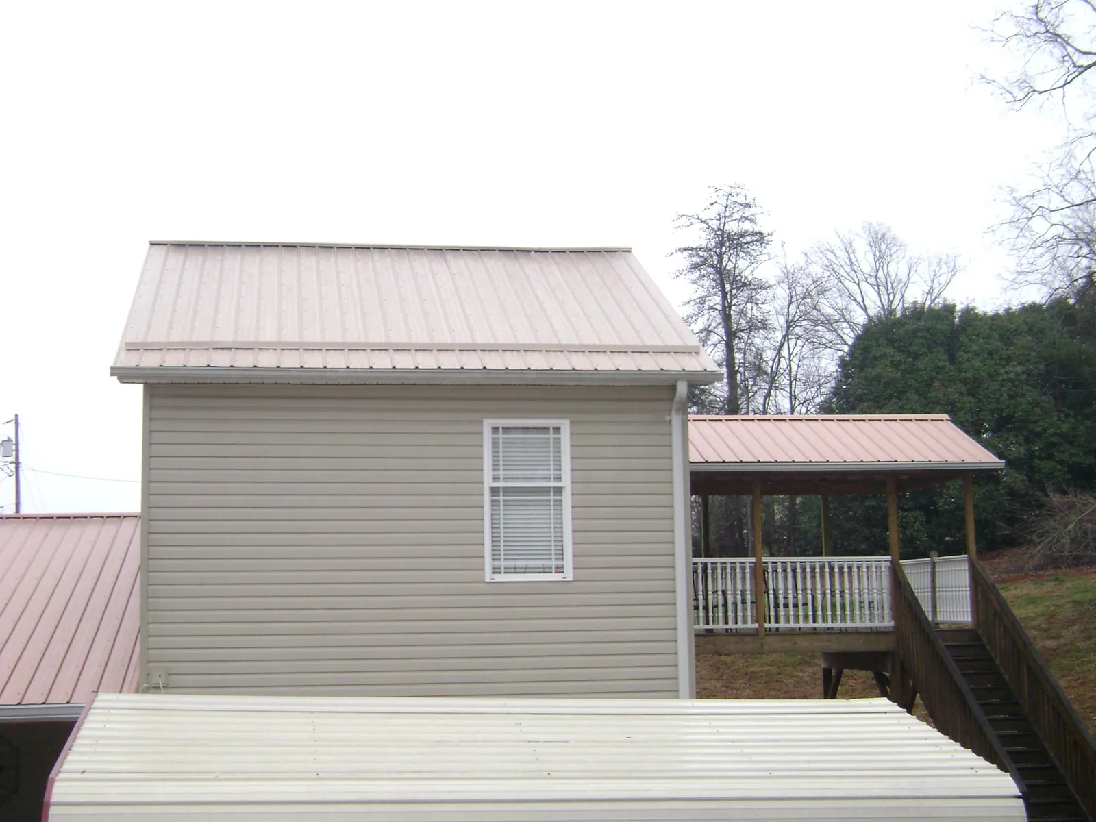Tan metal roofs on a two story addition and attached porch, from a Roof Replacement job in Richburg
